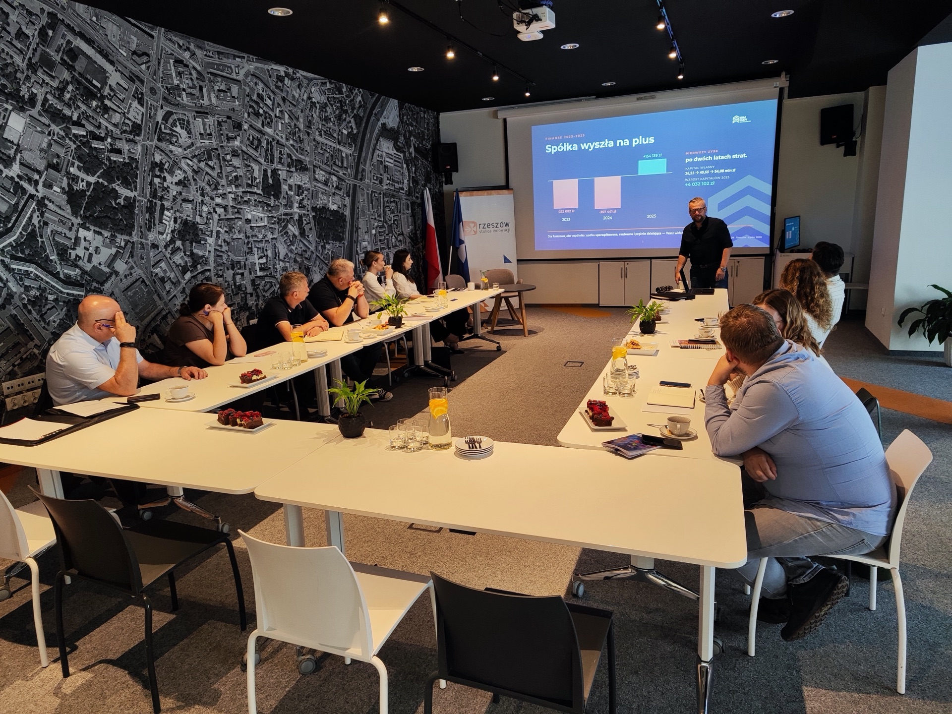 Uczestnicy spotkania roboczego SIM KZN Ziemi Podkarpackiej przy stole konferencyjnym w Urban Lab Rzeszów, w tle prezentacja spółki